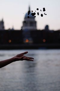 Cropped hand throwing stones against lake during sunset