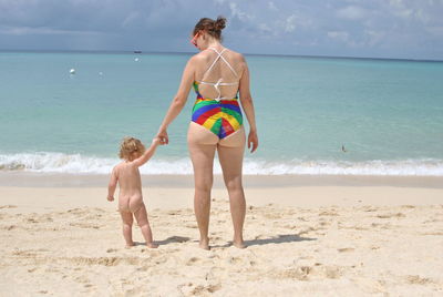 Rear view of shirtless boy standing on beach against sky