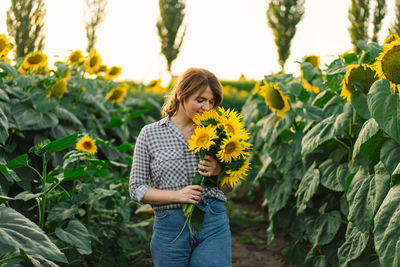 Beautiful young woman with sunflowers enjoying nature and laughing on summer sunflower field.