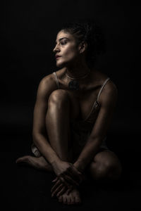 Woman looking away while sitting against black background