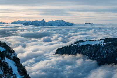 Aerial view of snow covered mountains and cloudscape against sky during winter