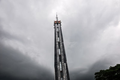 Low angle view of communications tower against cloudy sky