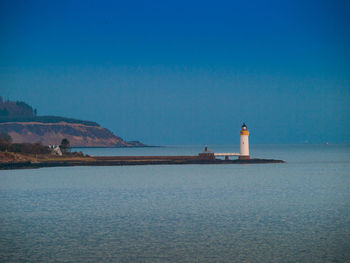 Lighthouse by sea and buildings against sky