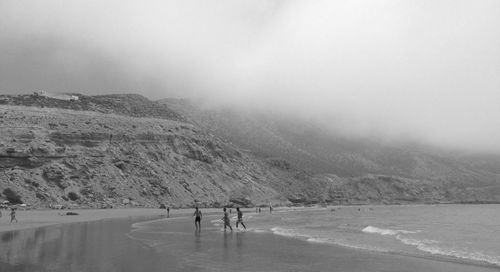 Scenic view of beach against mountain during fogy weather