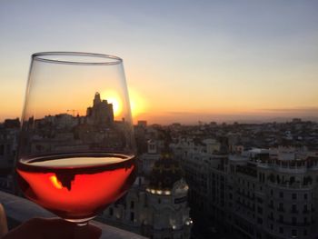 Close-up of beer in city against sky during sunset