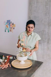 Woman with brown skin looking down, working on a flower arragement 