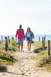 Happy couple with sunglasses holding hands while walking on beach