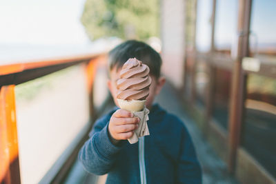 Boy holding ice cream cone while standing outdoors