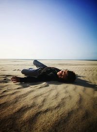 Man lying on sand at beach against sky