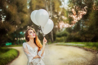 Young woman with balloons standing against trees