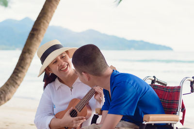 Smiling mother playing ukulele while sitting with son at beach