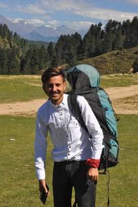 Front view of a happy young guy looking at camera with carrying parachute backpack in the mountain