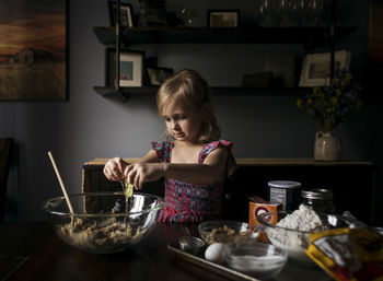Girl breaking eggs in bowl on table at home