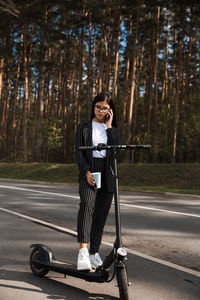 Woman talking over smart phone while standing on road against trees