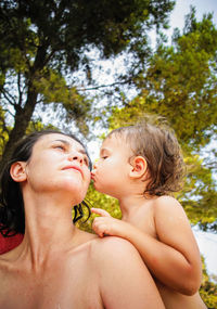 Close-up of boy kissing mother against trees