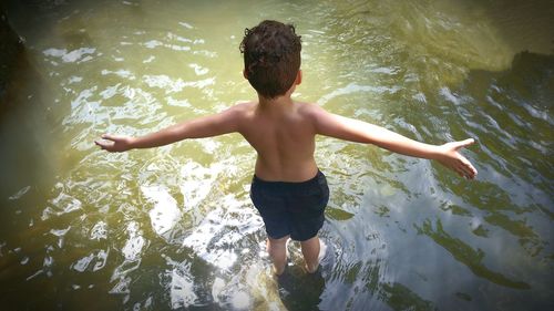 High angle view of shirtless boy with arms outstretched standing in lake