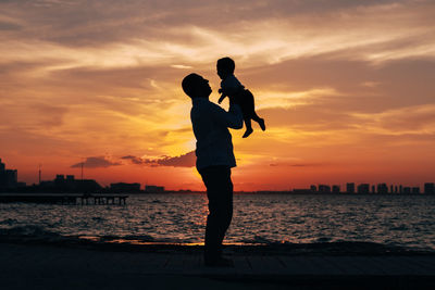 Silhouette man standing by sea against sky during sunset