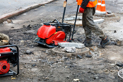 A road worker wearing orange vest repairs and installs sewers using a compactor plate,  jackhammer.