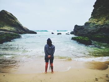 Rear view of woman standing at beach against sky