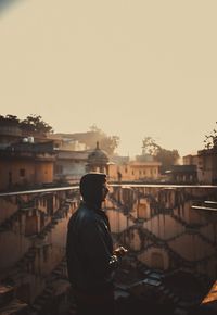 Rear view of man standing by railing against buildings