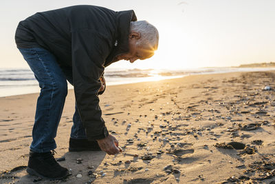 Senior man strolling at the beach, collecting shells