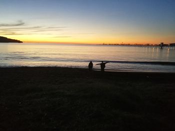 Silhouette people on beach against sky during sunset