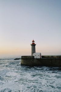 Lighthouse by sea against clear sky