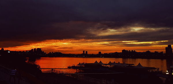 Silhouette city by river against sky during sunset