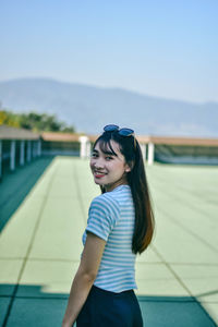 Portrait of cheerful young woman standing on building terrace against sky