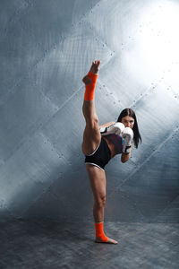 Full length of woman with arms raised against wall