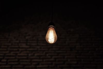Low angle view of illuminated light bulb hanging against black background