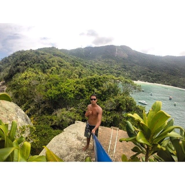 mountain, water, lifestyles, leisure activity, tranquility, beauty in nature, nature, scenics, lake, mountain range, tranquil scene, rock - object, sky, sitting, green color, young adult, plant, standing