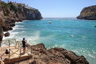 High angle view of man fishing at rocky sea shore against sky