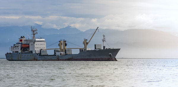 Large cargo container ship sailing against the volcano