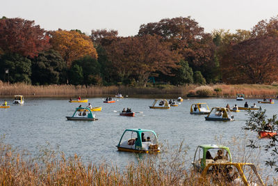 People in boats on sea against trees during sunset