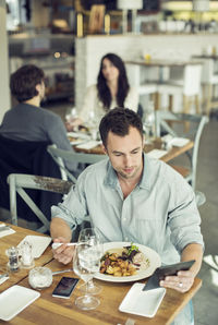 Mid adult businessman using digital tablet while having lunch in restaurant