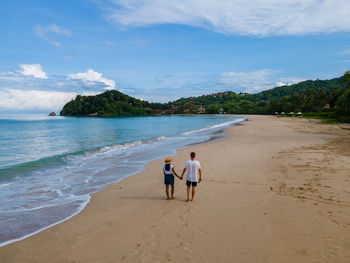 Rear view of woman walking at beach against sky