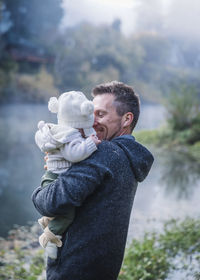 A man is holding a baby near a river