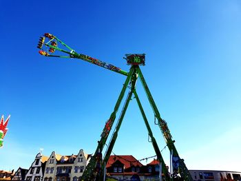 Low angle view of crane by building against clear blue sky