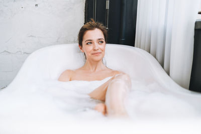 Young happy woman taking bath with foam at home, treat yourself