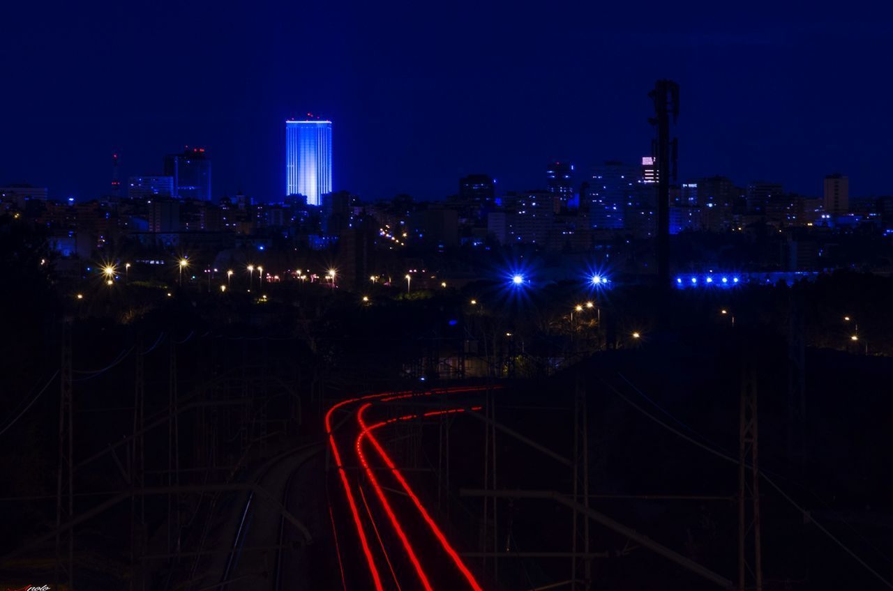 HIGH ANGLE VIEW OF ILLUMINATED RAILROAD TRACKS BY BUILDINGS AGAINST SKY