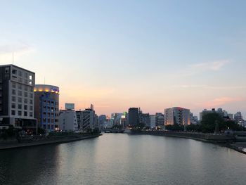 River by buildings in city against sky during sunset