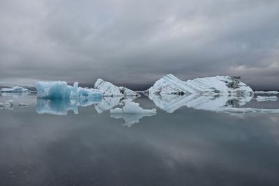 Scenic view of glaciers on lagoon against cloudy sky