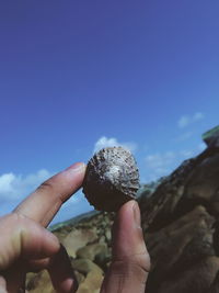 Cropped hand holding rock against blue sky