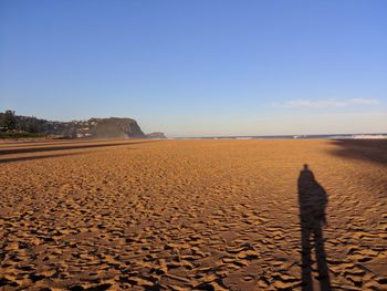 Shadow of person on sand at beach against clear sky