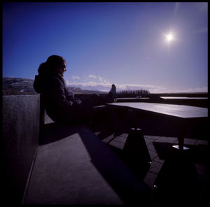 Side view of woman sitting on table against clear sky