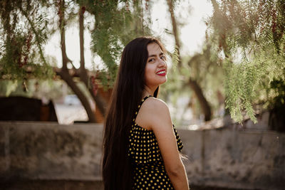 Portrait of smiling young woman standing against trees