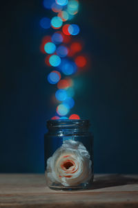 Rose in jar against illuminated defocused lights on table