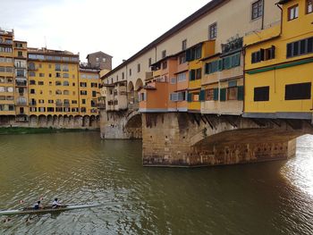 Bridge over canal by buildings in city against sky