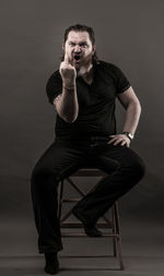 Mid adult man gesturing obscene gesture while sitting against black background